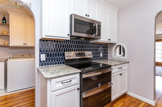 kitchen with appliances with stainless steel finishes, washer / dryer, white cabinetry, and light hardwood / wood-style flooring