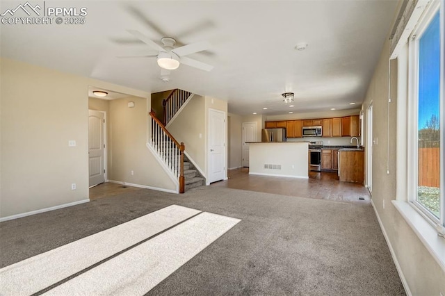 unfurnished living room featuring ceiling fan, dark carpet, and sink