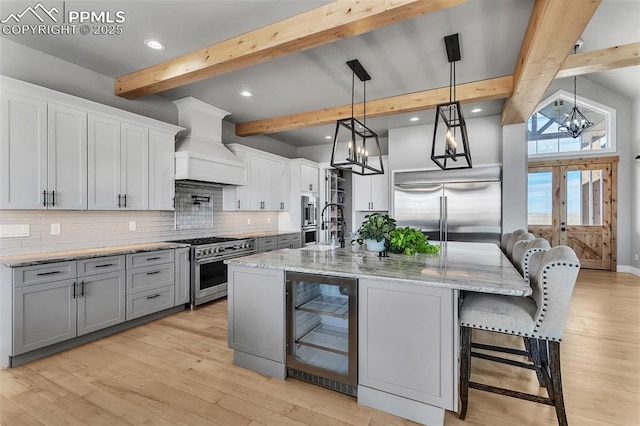 kitchen featuring premium range hood, high end appliances, hanging light fixtures, a kitchen island with sink, and beverage cooler