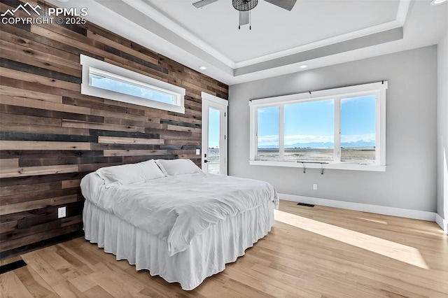 bedroom with ceiling fan, a tray ceiling, light hardwood / wood-style flooring, and wooden walls