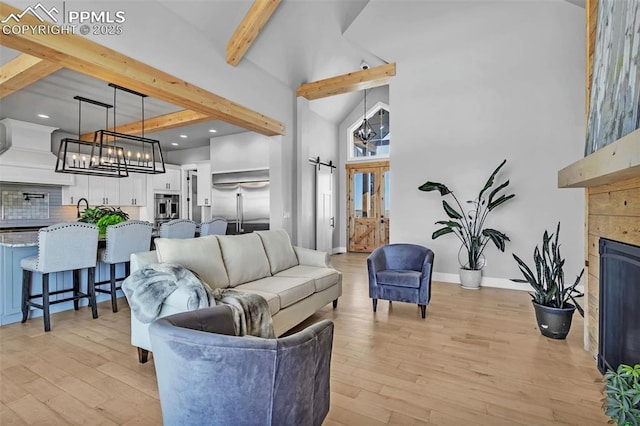 living room featuring a towering ceiling, beamed ceiling, an inviting chandelier, light wood-type flooring, and a tiled fireplace