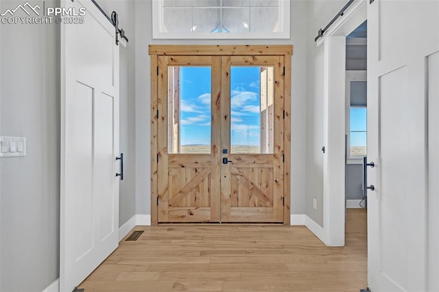 foyer with a barn door, french doors, and light hardwood / wood-style flooring