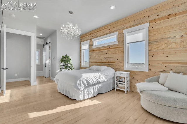 bedroom featuring connected bathroom, wood walls, a chandelier, light hardwood / wood-style flooring, and a barn door