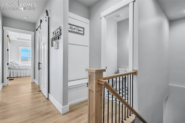 corridor with a barn door and light hardwood / wood-style flooring