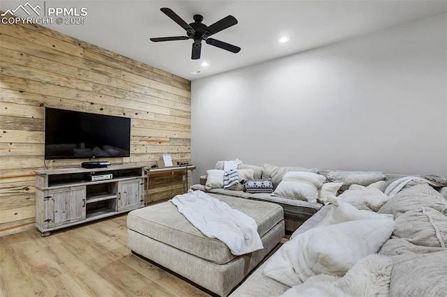 living room featuring ceiling fan, light hardwood / wood-style floors, and wood walls