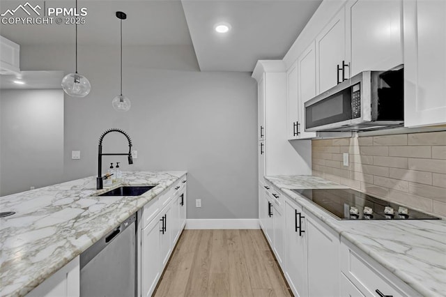 kitchen featuring light stone countertops, white cabinetry, stainless steel appliances, sink, and hanging light fixtures