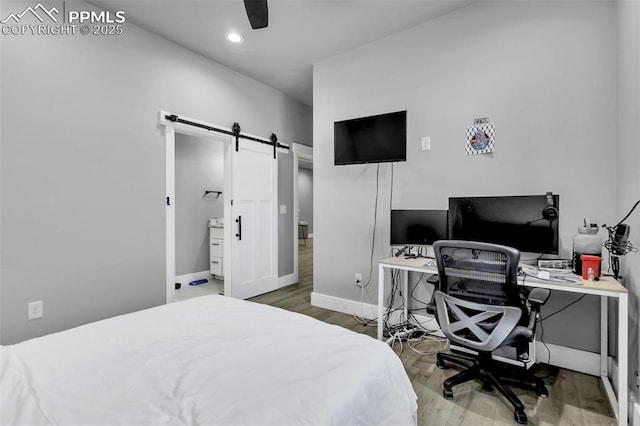 bedroom featuring ceiling fan, a barn door, and wood-type flooring