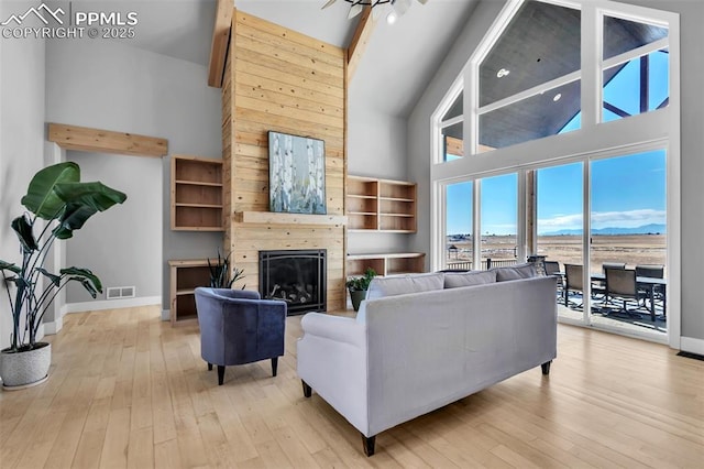 living room with ceiling fan, light hardwood / wood-style floors, beam ceiling, a large fireplace, and high vaulted ceiling