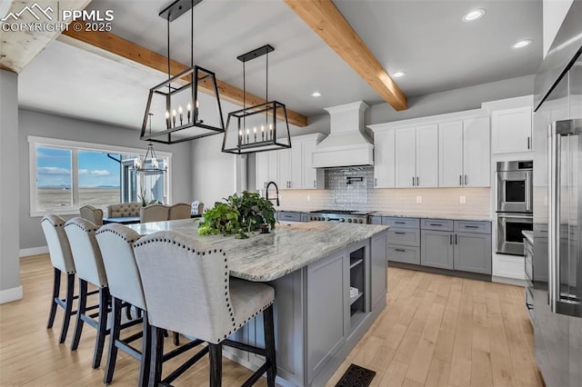 kitchen with decorative light fixtures, white cabinetry, a large island with sink, and custom exhaust hood