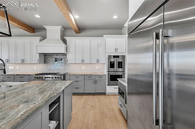 kitchen with light wood-type flooring, beamed ceiling, premium range hood, and stainless steel appliances