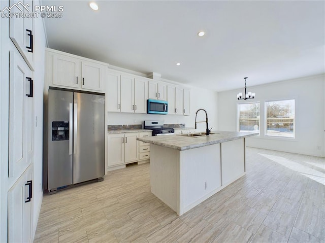 kitchen featuring pendant lighting, appliances with stainless steel finishes, white cabinetry, sink, and a kitchen island with sink