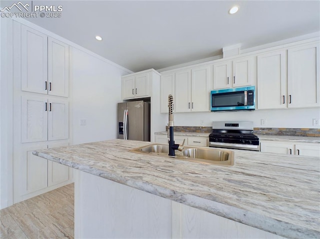 kitchen featuring white cabinets, appliances with stainless steel finishes, sink, light wood-type flooring, and light stone counters