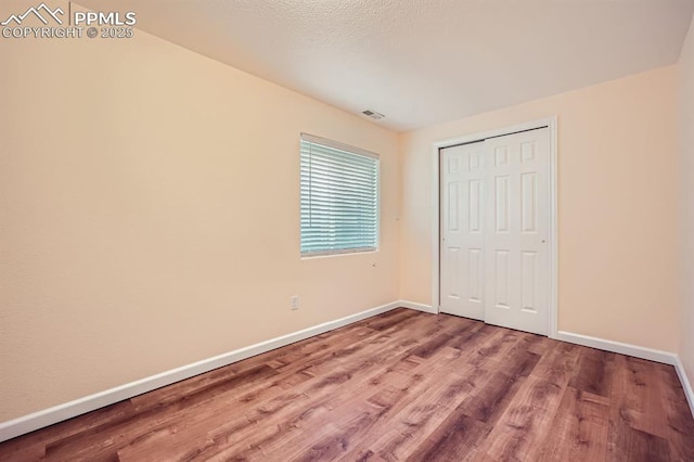 unfurnished bedroom with baseboards, a closet, visible vents, and wood finished floors