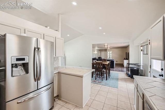 kitchen with kitchen peninsula, stainless steel fridge, lofted ceiling, white cabinets, and light tile patterned flooring