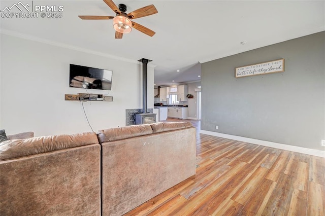 living room with ceiling fan, light hardwood / wood-style floors, crown molding, and a wood stove