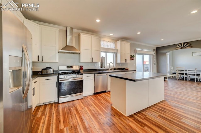 kitchen featuring wall chimney exhaust hood, stainless steel appliances, light hardwood / wood-style floors, a kitchen island, and white cabinets