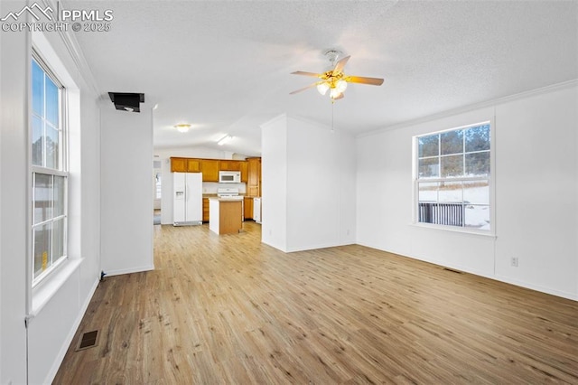 unfurnished living room featuring ceiling fan, vaulted ceiling, a healthy amount of sunlight, and light wood-type flooring