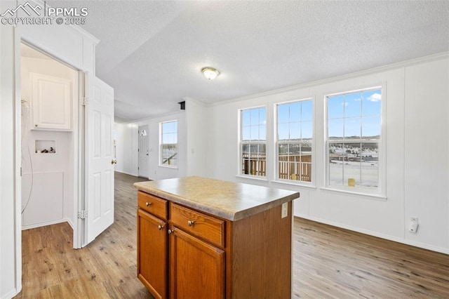 kitchen featuring crown molding, a center island, a textured ceiling, and light wood-type flooring