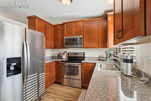 kitchen with light stone countertops, lofted ceiling, stainless steel appliances, sink, and light wood-type flooring