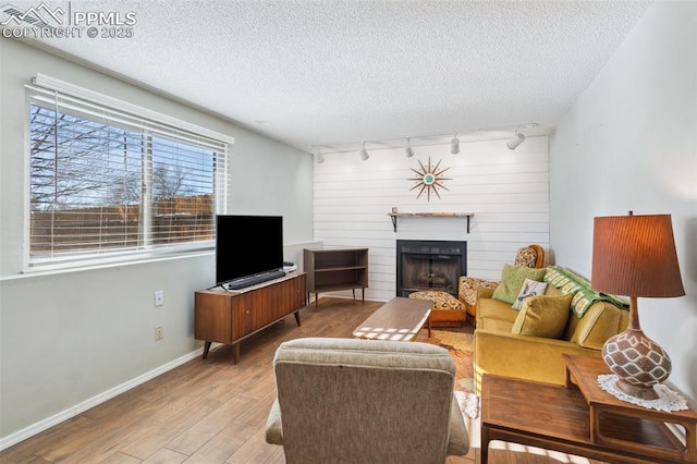 living room featuring a textured ceiling, a large fireplace, rail lighting, and light hardwood / wood-style floors