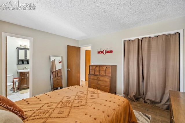 bedroom featuring light hardwood / wood-style floors, a textured ceiling, and ensuite bath