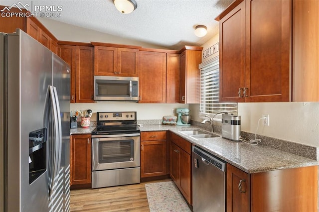 kitchen with appliances with stainless steel finishes, a textured ceiling, vaulted ceiling, light hardwood / wood-style flooring, and sink