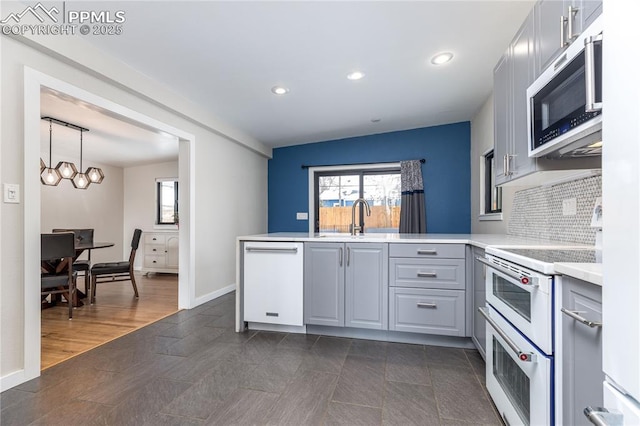 kitchen featuring hanging light fixtures, sink, gray cabinetry, white appliances, and decorative backsplash