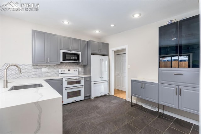 kitchen with white appliances, light stone countertops, sink, backsplash, and gray cabinets