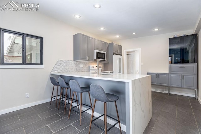 kitchen with high quality fridge, stainless steel range, decorative backsplash, gray cabinets, and kitchen peninsula