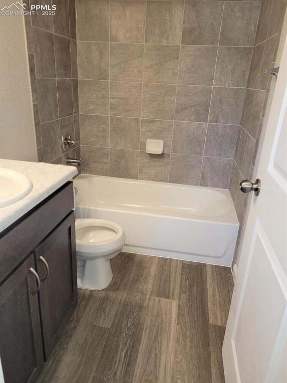 full bathroom featuring hardwood / wood-style floors, tiled shower / bath combo, vanity, and toilet