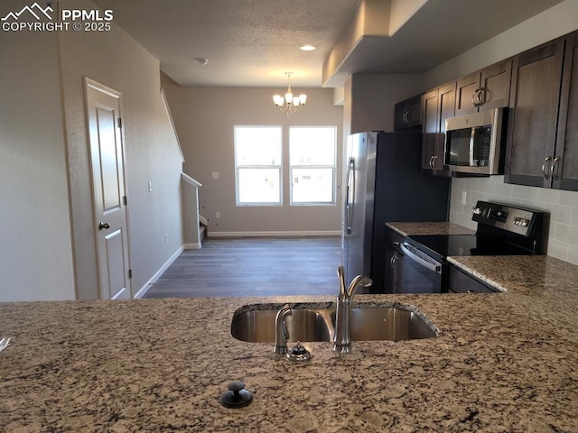 kitchen featuring a chandelier, sink, backsplash, stainless steel appliances, and light stone counters