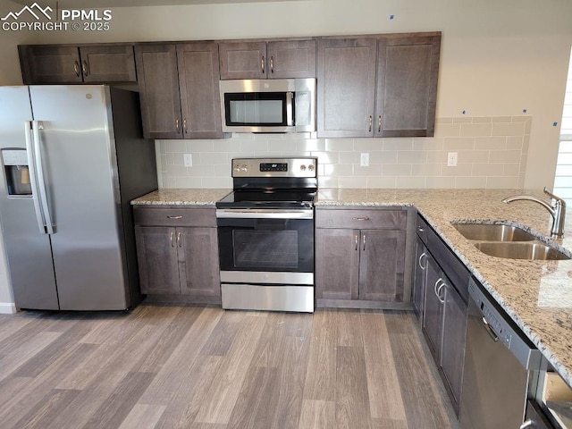 kitchen with sink, backsplash, light stone counters, and appliances with stainless steel finishes