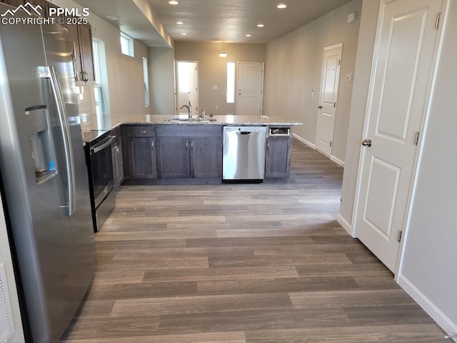 kitchen featuring hardwood / wood-style flooring, dark brown cabinets, sink, stainless steel appliances, and light stone counters