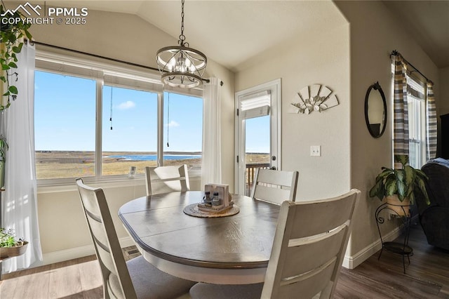 dining space featuring lofted ceiling, a water view, an inviting chandelier, and hardwood / wood-style floors