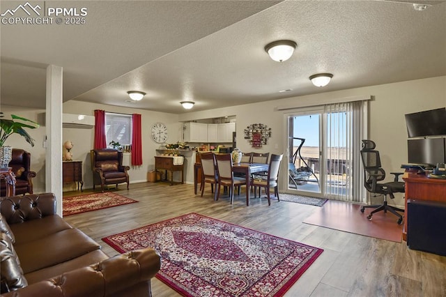 living room featuring an AC wall unit, a textured ceiling, and light hardwood / wood-style floors