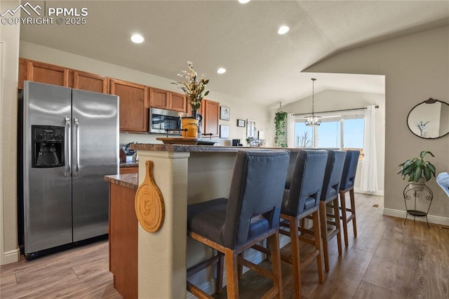 kitchen with a center island, stainless steel appliances, a kitchen breakfast bar, hanging light fixtures, and vaulted ceiling