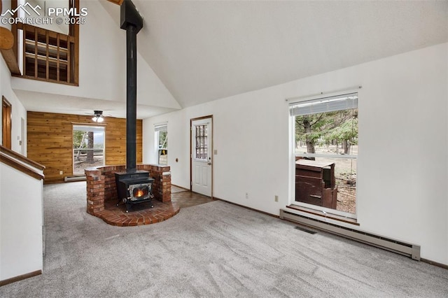 living room with baseboard heating, carpet flooring, wooden walls, and high vaulted ceiling