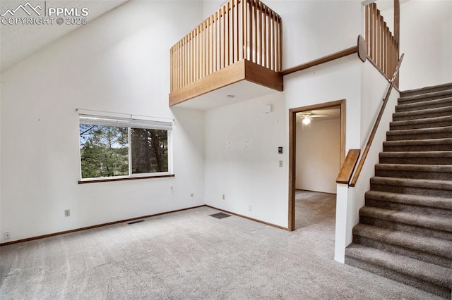 unfurnished living room featuring ceiling fan, carpet flooring, and a towering ceiling