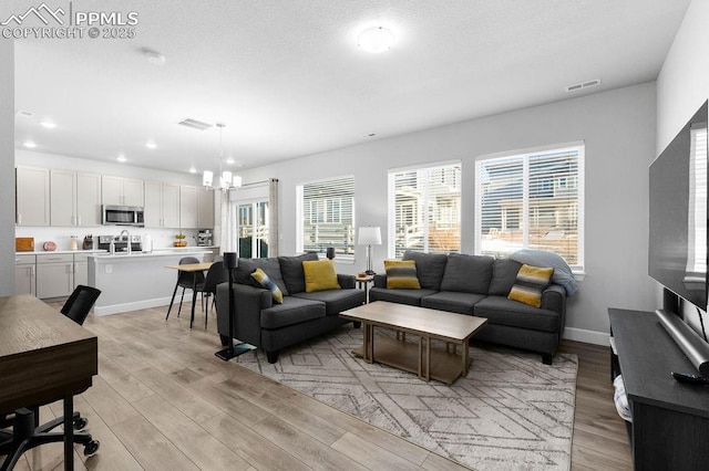 living room with plenty of natural light, a chandelier, and light wood-type flooring