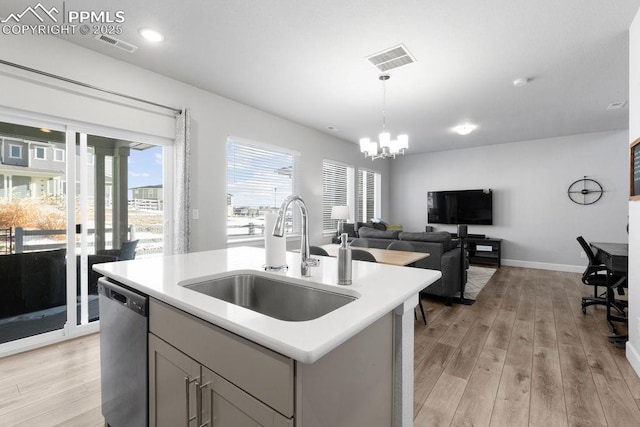 kitchen featuring an island with sink, sink, a notable chandelier, stainless steel dishwasher, and gray cabinetry