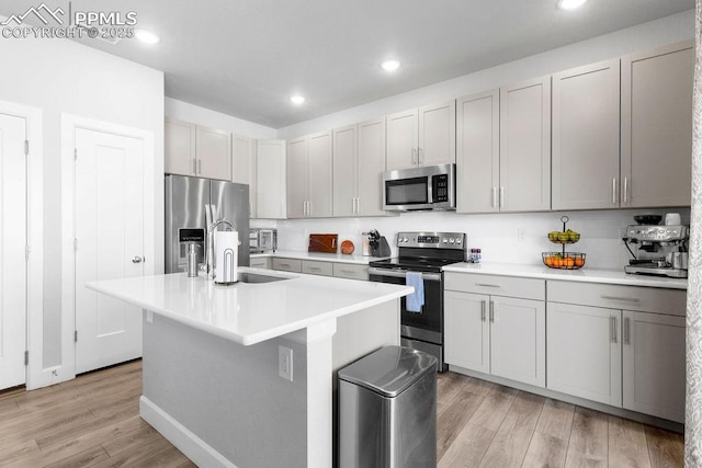 kitchen with light wood-type flooring, appliances with stainless steel finishes, an island with sink, and sink