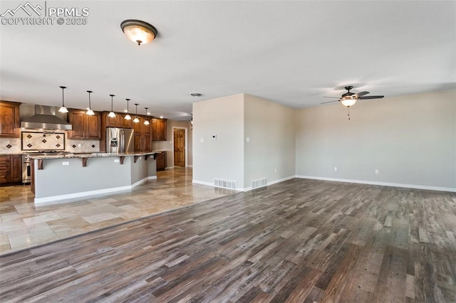 kitchen featuring a kitchen bar, stainless steel appliances, tasteful backsplash, hanging light fixtures, and wall chimney exhaust hood