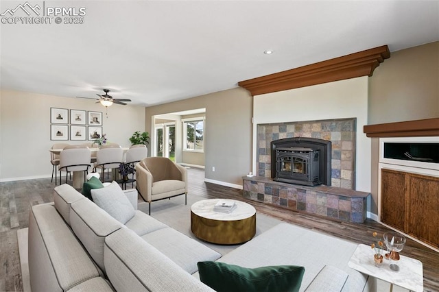 living room with ceiling fan, a wood stove, and hardwood / wood-style flooring