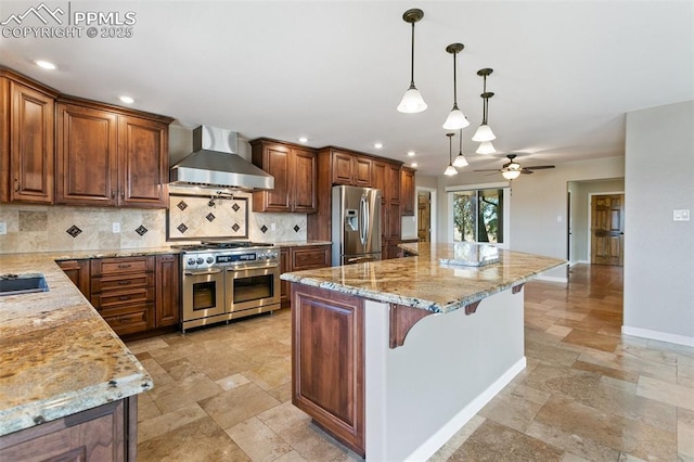 kitchen with appliances with stainless steel finishes, decorative light fixtures, light stone countertops, a kitchen island, and wall chimney range hood