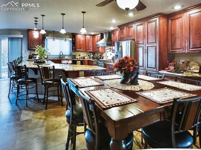 kitchen with a healthy amount of sunlight, wall chimney exhaust hood, hanging light fixtures, and stainless steel refrigerator