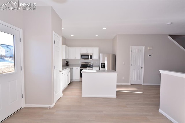 kitchen featuring white cabinets, light wood-type flooring, stainless steel appliances, and a center island