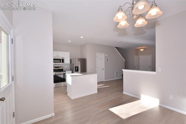 kitchen with a center island, white cabinetry, stainless steel appliances, hanging light fixtures, and a notable chandelier