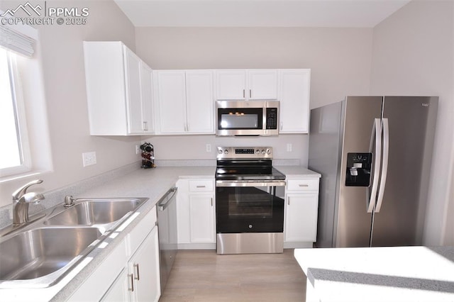 kitchen with light wood-type flooring, appliances with stainless steel finishes, sink, and white cabinetry