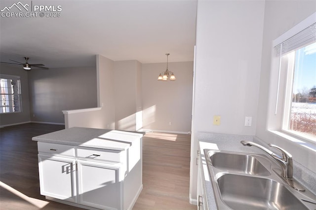 kitchen with white cabinetry, hardwood / wood-style flooring, pendant lighting, ceiling fan with notable chandelier, and sink