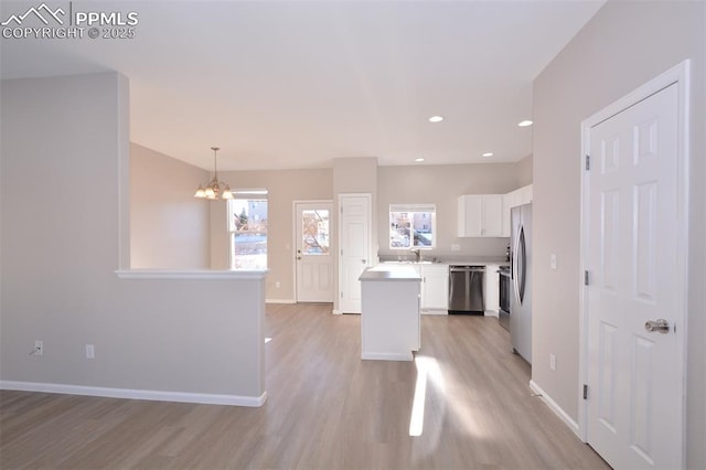 kitchen with white cabinetry, appliances with stainless steel finishes, a kitchen island, hanging light fixtures, and a chandelier